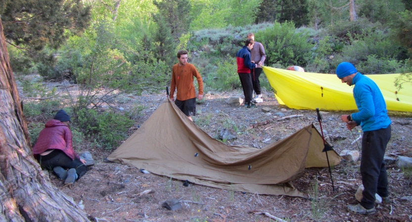a group of outward bound students work to set up tarp shelters 